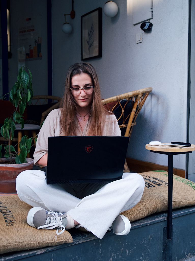 Woman sitting cross-legged with laptop, focusing in cozy cafe environment. Relaxed and productive atmosphere.